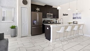A modern kitchen with dark cabinets, stainless steel appliances, and a white island with bar stools. - 5BR Home w/ Private Pool - Storey Lake Resort (Kissimmee)