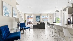 A modern living room with a sofa, a dining table, and a kitchen area with a bar. - 5BR Home w/ Private Pool - Storey Lake Resort (Kissimmee)