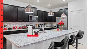 A modern kitchen with dark cabinets, stainless steel appliances, and a marble island with bar stools. - Themed 5BR Home + Pool at Windsor Cay (Clermont)