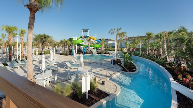 A resort pool area with a water slide, lounge chairs, and palm trees. - Themed 5BR Home + Pool at Windsor Cay (Clermont)