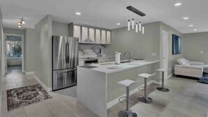 Une cuisine moderne dotée d’un îlot central, d’appareils électroménagers en acier inoxydable et de luminaires suspendus.