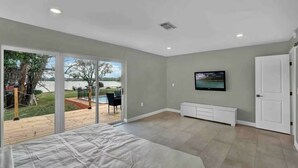 Une chambre avec un lit, une télévision, une porte-fenêtre coulissante donnant sur une terrasse, et une vue sur une piscine et des arbres.