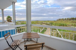 A balcony with a wooden table and two chairs, overlooking a grassy landscape and the sea. - Sea Apartment - with shared Pool (Villaggio del Golfo)