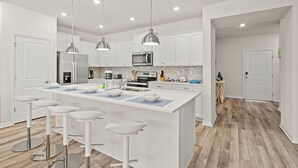 Une cuisine moderne avec des meubles blancs, des appareils en acier inoxydable et des tabourets de bar.