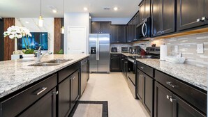 Una cocina moderna con armarios oscuros, encimeras de granito, electrodomésticos de acero inoxidable y una isla grande con pileta.