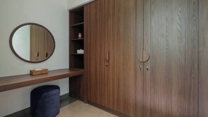 Una habitación con un armario de madera, un espejo redondo, un banco de madera y un cubo de basura.