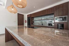 A modern kitchen with a marble countertop, wooden cabinets, and built-in appliances. - Villa Jenggala by GORO (Kabupaten Gianyar)