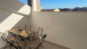 Eine kleine Terrasse im Freien mit einem Holztisch und Stühlen, einer gewebten Tischmatte und einem Glas Drink.