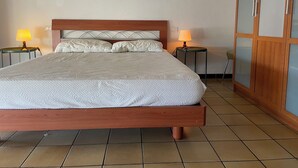 Ein ordentlich bezogenes Bett mit Holz-Kopfteil, zwei Nachttische mit Lampen sowie ein Holzschrank mit Glastüren.
