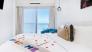 Una camera d'albergo con un letto, vista sul mare attraverso ampie finestre e un balcone.