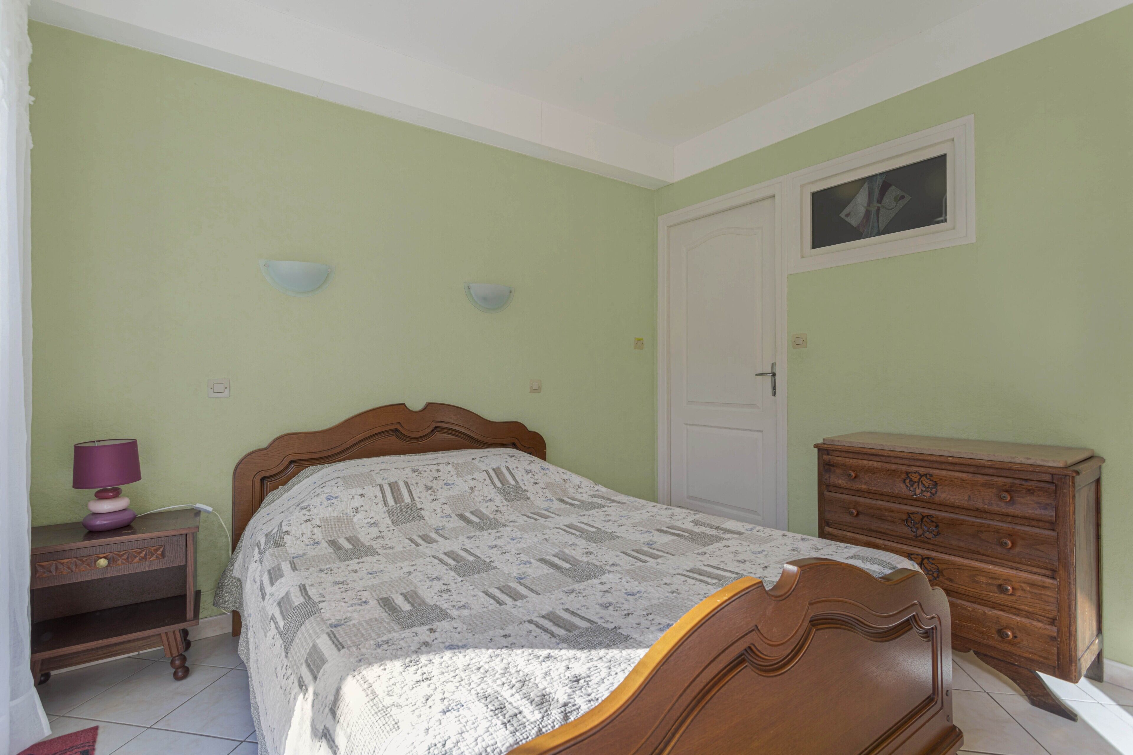 A bedroom with a bed, dresser, nightstand, and wall sconces.