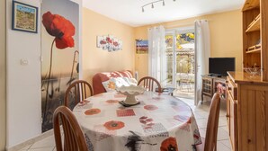 A dining area with a table set for four, a large flower painting on the wall, and a view through a glass door to an outdoor area. - Apartment 'À Ria-sirach' with Mountain View, Shared Terrace and Wi-Fi (Ria-Sirach)