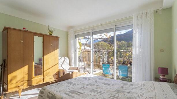 A bedroom with a bed, a wardrobe, a chair, and a view through a large window. - Apartment 'À Ria-sirach' with Mountain View, Shared Terrace and Wi-Fi (Ria-Sirach)
