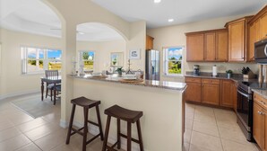 A spacious kitchen with wooden cabinets, a large island with stools, and a view of the outdoors through the windows. - Seaside Villa Golfers Delight South facing, quiet location, privacy, heated pool (Cape Coral)