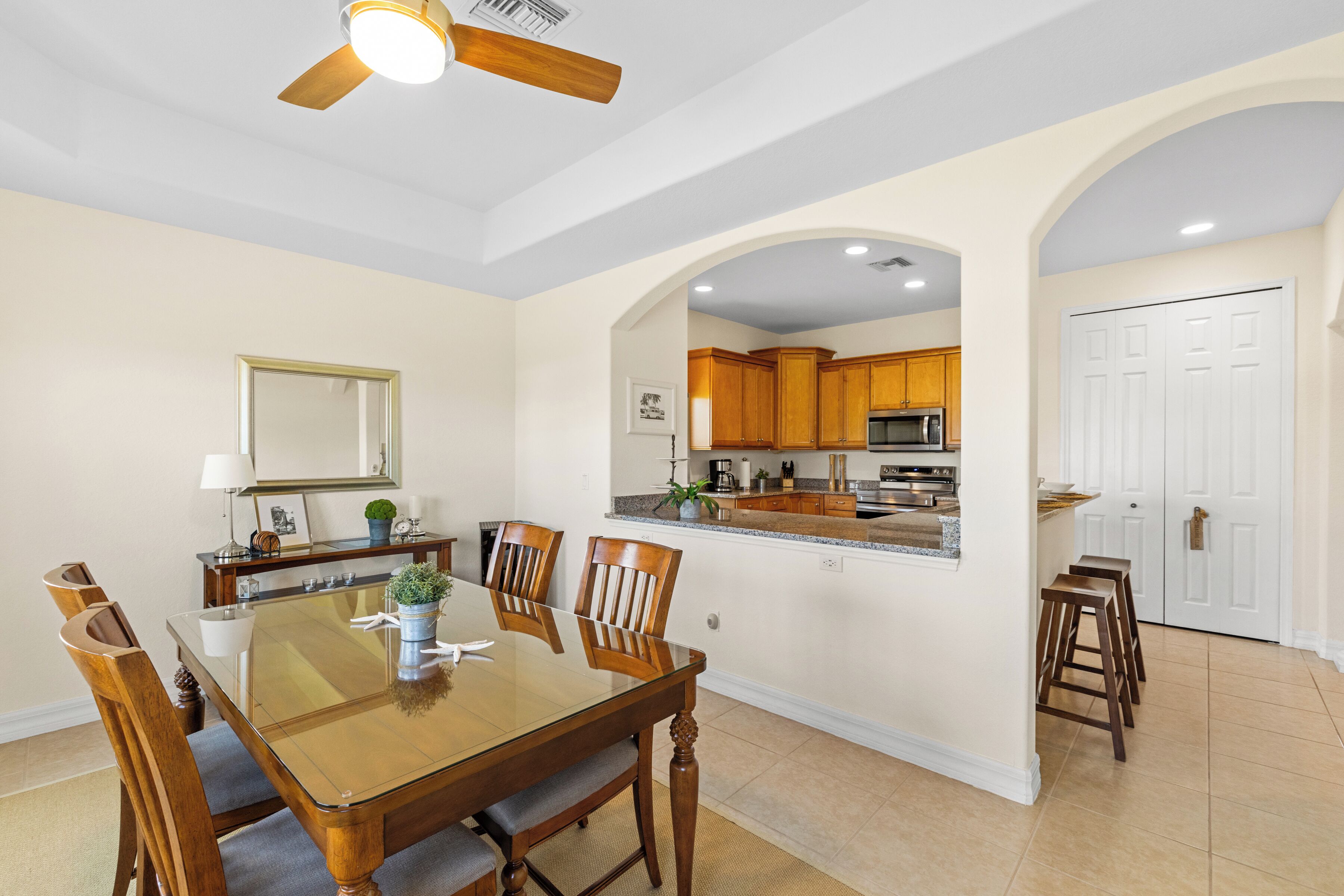 A dining area with a glass-top table, wooden chairs, and a ceiling fan.