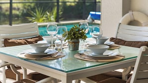 A dining table with glass top, white chairs, and a view of a swimming pool. - Seaside Villa Golfers Delight South facing, quiet location, privacy, heated pool (Cape Coral)