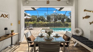 A dining area with a glass table, chairs, and a view of a swimming pool. - Seaside Villa Golfers Delight South facing, quiet location, privacy, heated pool (Cape Coral)