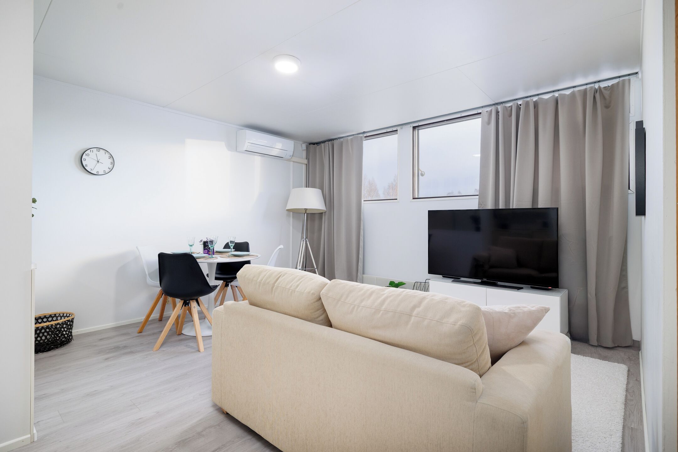 Sala de estar moderna com sofá, televisão, espaço de jantar com mesa e cadeiras, e uma janela grande com cortinas.
