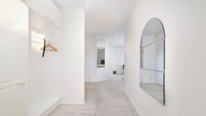 Un pasillo con paredes blancas, suelo de madera, un perchero colgante y un espejo grande en la pared derecha.