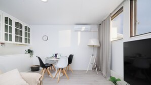 Una sala de estar moderna con un sofá, una mesa de comedor con sillas, un televisor y una ventana con cortinas.