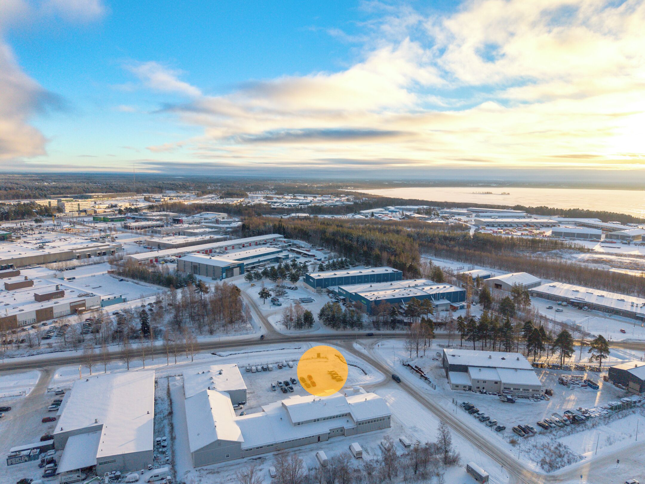 An aerial view of a commercial area with multiple buildings, parking lots, and a body of water in the background.