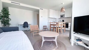 Et moderne hotelværelse med seng, skrivebord, spisebord med stole, fjernsyn og et tekøkken.