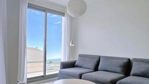 En moderne stue med en grå sofa, et hvidt sofabord og en stor skydedør til et udendørs område.