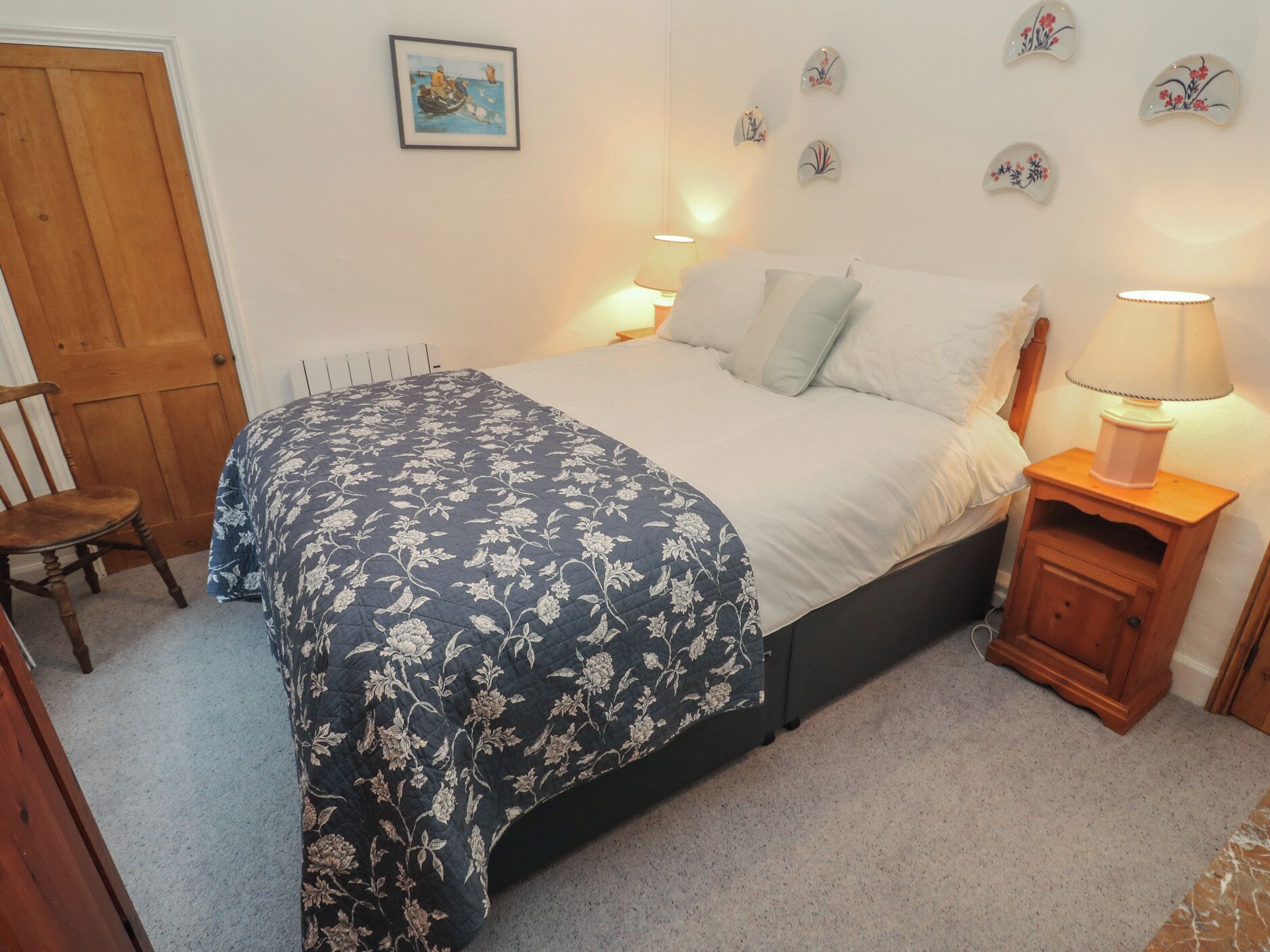 Een slaapkamer met een bed, een stoel, een nachtkastje met een lamp en decoratieve wandkunst.