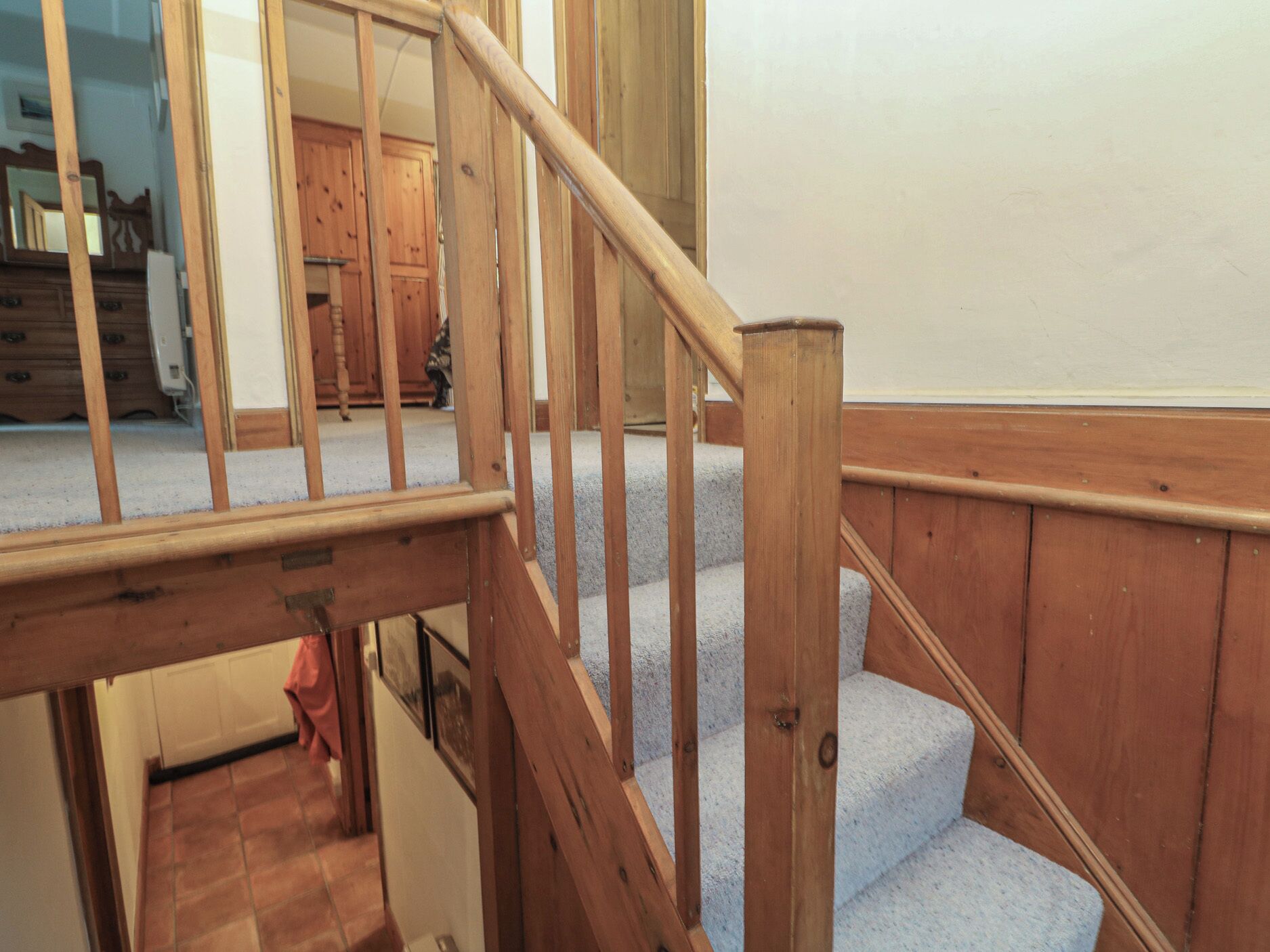 A wooden staircase with a handrail, carpeted steps, and a view of a room with wooden cabinets and a tiled floor.