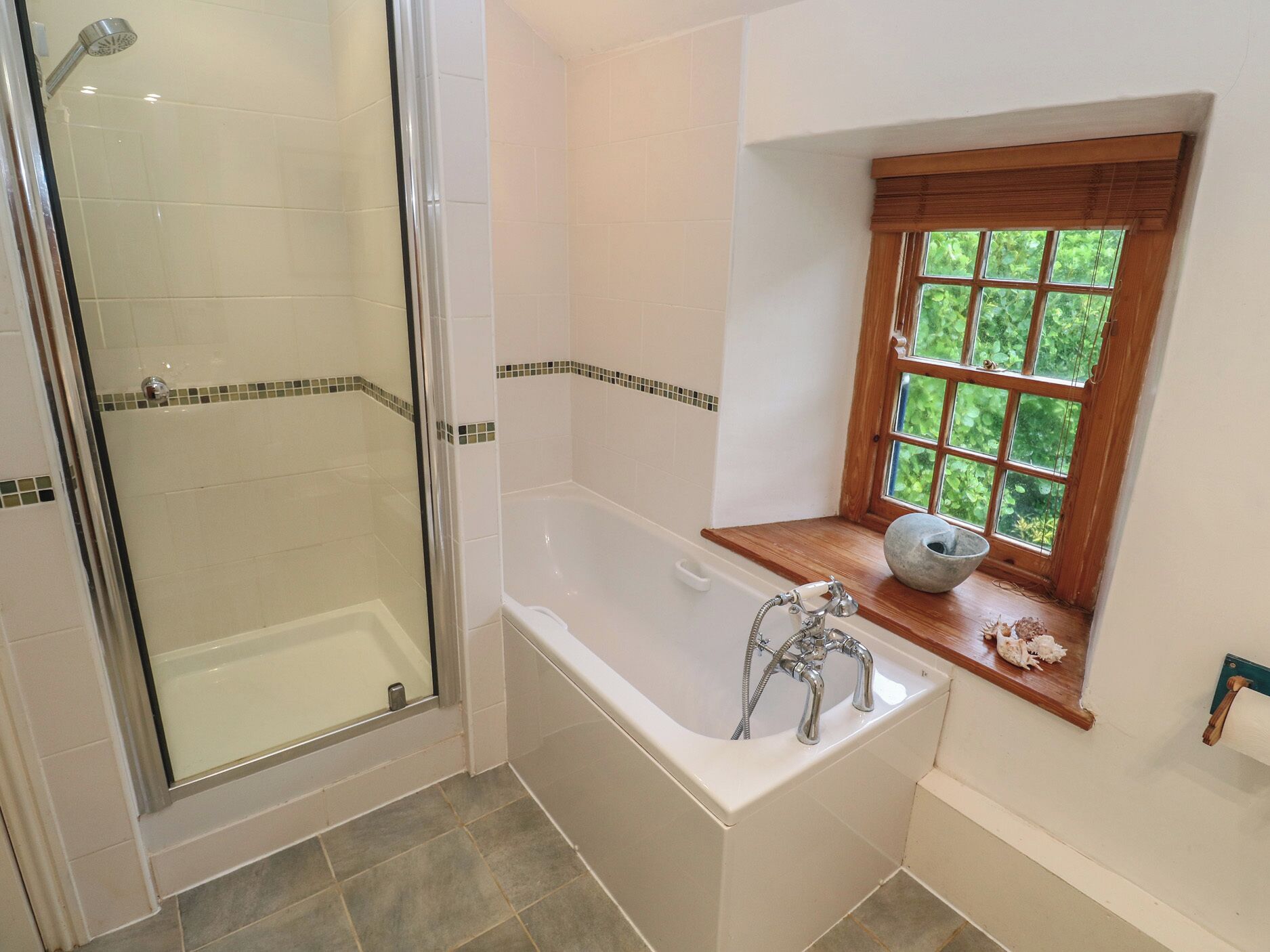 Une salle de bain dotée d’une douche à parois de verre, d’une baignoire sur pieds et d’une fenêtre donnant sur un paysage verdoyant.