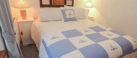 A neatly made bed with a checkered bedspread featuring sailboat designs, flanked by two bedside lamps on white nightstands.