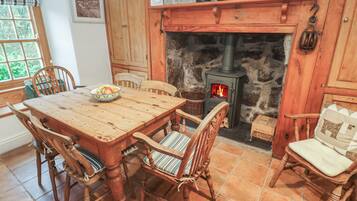 A rustic wooden dining area with a stone fireplace, wooden chairs, and a table set with a bowl of fruit.