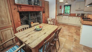 Una cocina rústica con pared de piedra, armarios de madera y una estufa de leña en el centro.