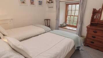 Une chambre avec deux lits, une commode en bois, une fenêtre avec des rideaux et des œuvres d’art accrochées au mur.