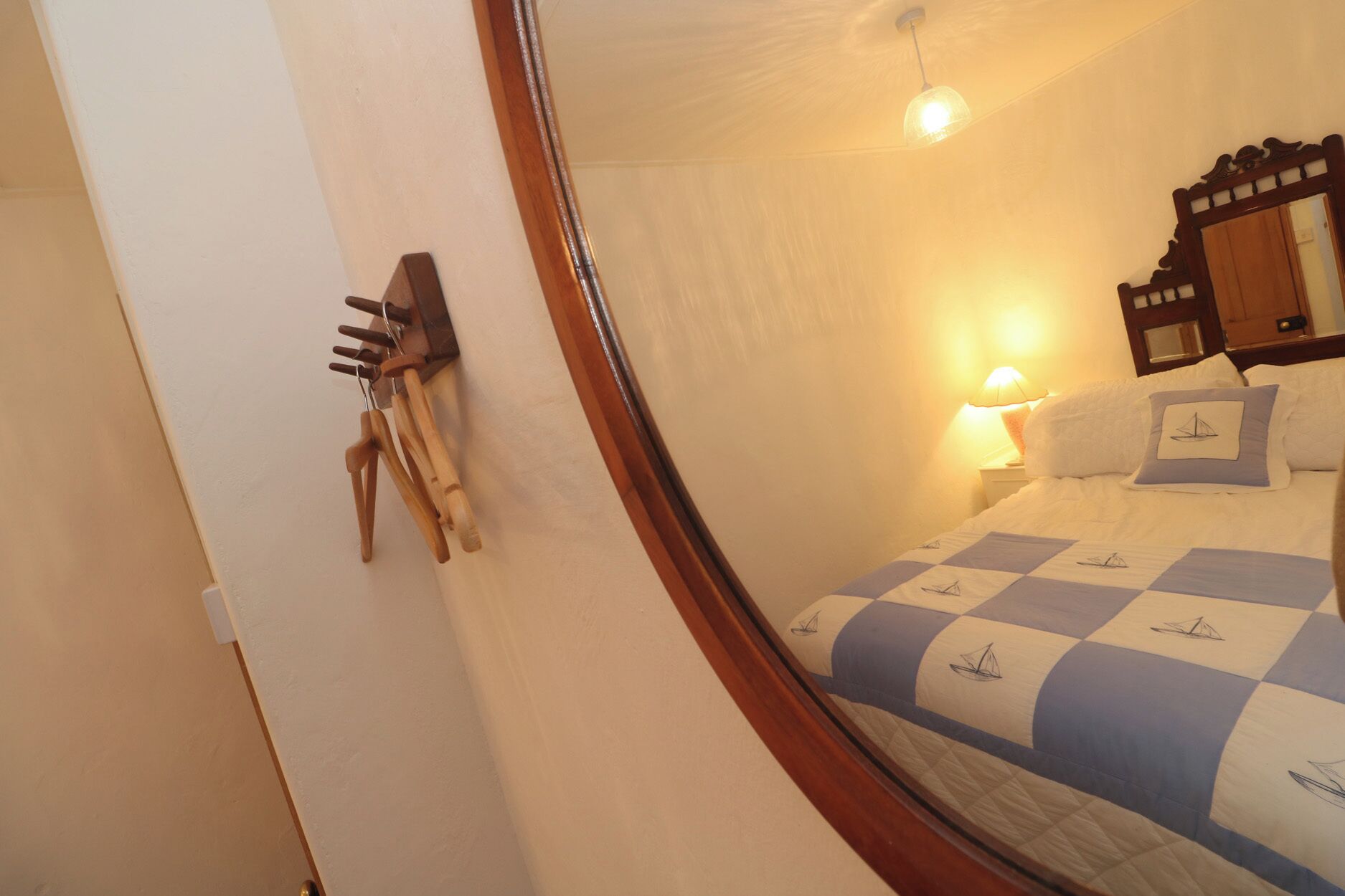 A bedroom with a bed, a nightstand, a mirror, and a wall-mounted rack with keys.