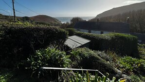 Un paisaje costero con una casa que domina el mar, rodeada de vegetación y colinas.
