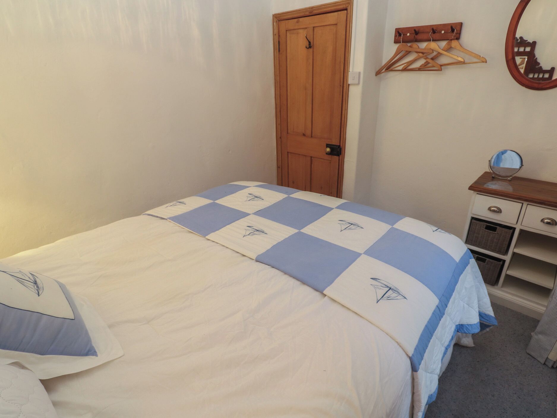 A bedroom with a bed, a wooden door, a dresser with drawers, and a mirror.