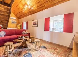 A cozy living room with a red sofa, wooden floor, and a window with red shutters. - Cupidon Guest Room with Mountain View, Wi-Fi, and Air Conditioning (Singles)