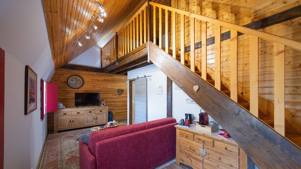 A wooden interior with a staircase, a red sofa, a television, and a wooden cabinet.