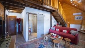 A wooden interior with a red sofa, a staircase, and a view of the outside.