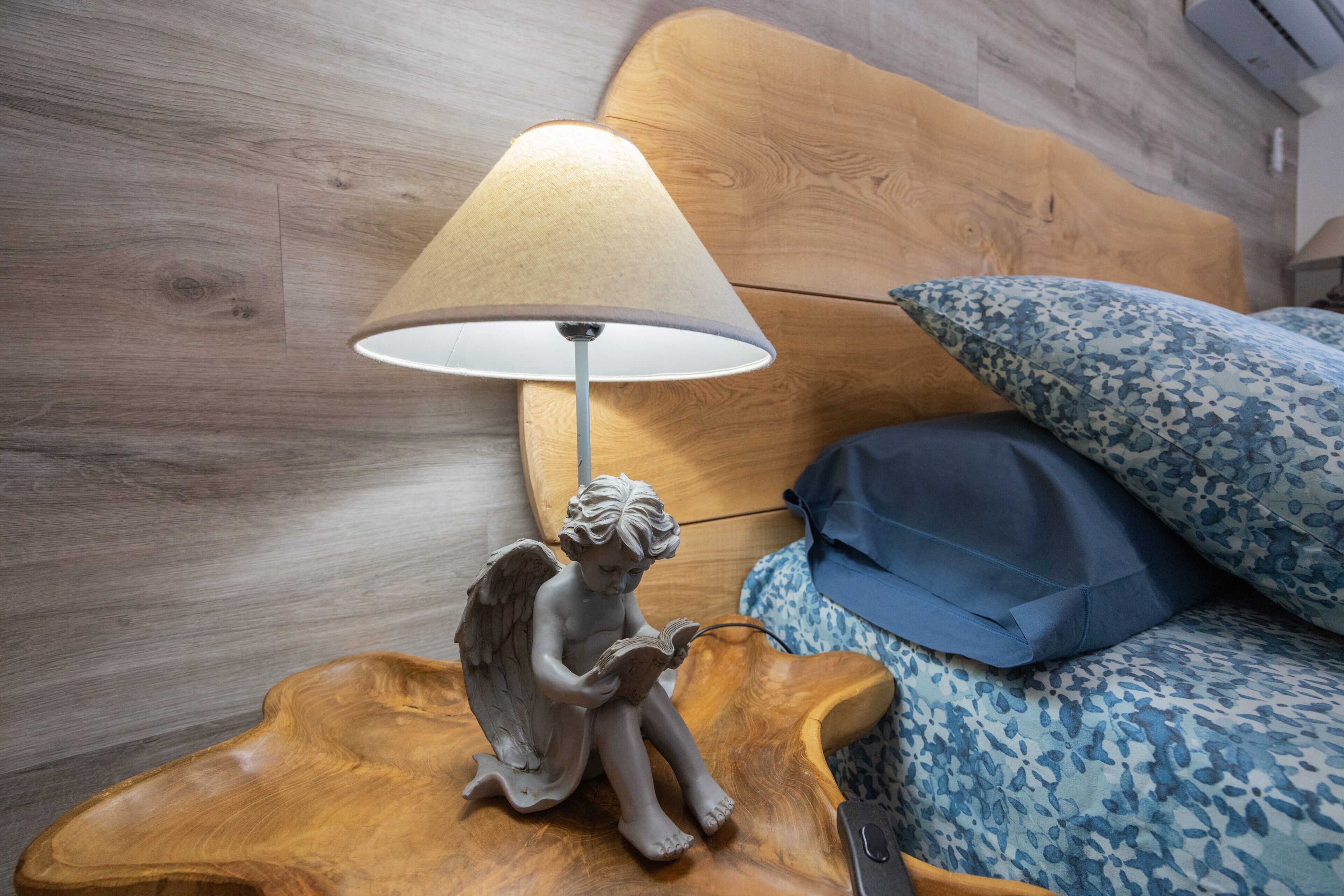 A wooden nightstand with a lamp, a decorative angel figurine, and a bed with patterned bedding.