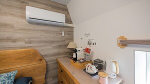 Ein Zimmer mit einem Bett mit Holz-Kopfteil, einer Holzkommode, einer Kaffeemaschine, einem Wasserkocher und einer wandmontierten Klimaanlage.