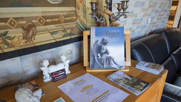 A reception desk with a book titled 'Le mystère des Anges' and a small statue of an angel. - “Chambre Raphaël” Guest Room with Mountain View, Wi-Fi, and Air Conditioning (Singles)