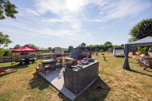 An outdoor patio area with a stone barbecue station, seating arrangements, and a red canopy tent. - “Chambre Raphaël” Guest Room with Mountain View, Wi-Fi, and Air Conditioning (Singles)