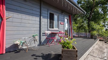 A wooden deck with a bicycle, a red chair, and a planter with green plants.