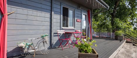 Eine Holzterrasse mit einem Fahrrad, einem roten Stuhl und einem Blumentopf mit grünen Pflanzen.