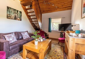 A living room with a brown leather sofa, a wooden coffee table, a TV, and a staircase. - “Chambre Raphaël” Guest Room with Mountain View, Wi-Fi, and Air Conditioning (Singles)