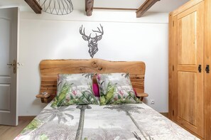 A bedroom with a wooden headboard, a bed with a tropical print bedspread, a wall-mounted deer head decoration, and a wooden wardrobe. - “Chambre Raphaël” Guest Room with Mountain View, Wi-Fi, and Air Conditioning (Singles)