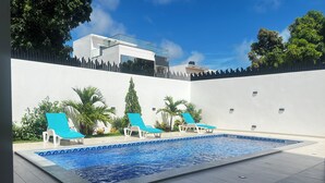 A swimming pool with lounge chairs and a modern building in the background. - Teranga Blue (Ngaparou)