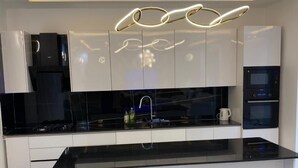 A modern kitchen with a black countertop, white cabinets, and a unique ceiling light fixture. - Teranga Blue (Ngaparou)